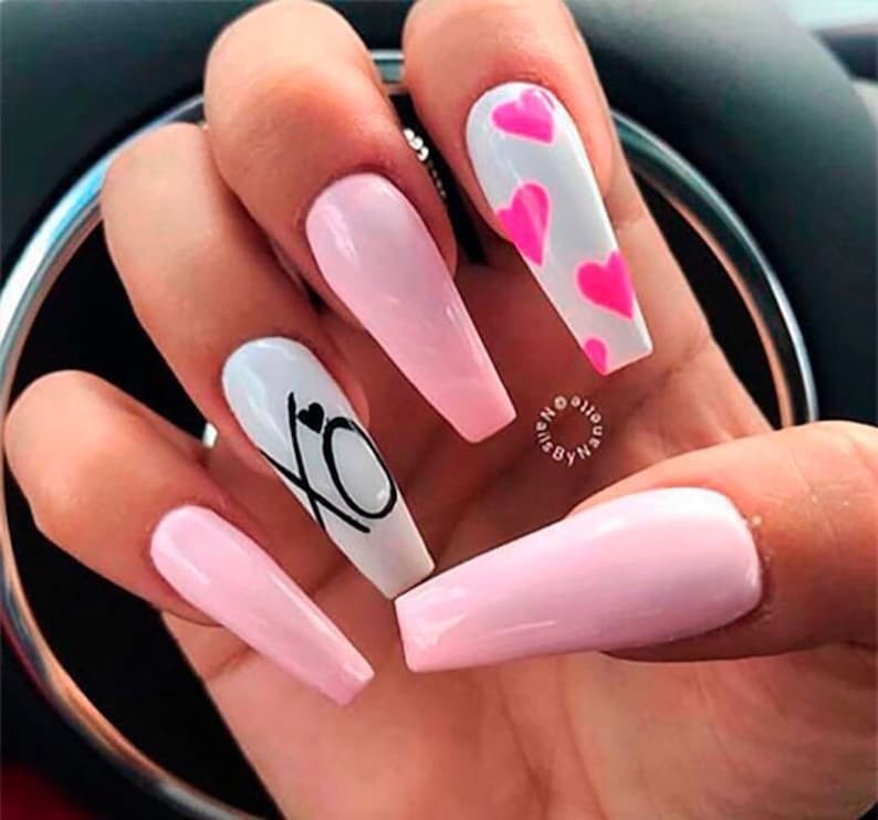 Puede incluir: U&ntilde;as acr&iacute;licas largas en forma de almendra, de color rosa y blanco, con un dise&ntilde;o de corazones rosas en una u&ntilde;a y las letras XO con un peque&ntilde;o coraz&oacute;n en otra u&ntilde;a.