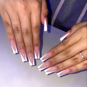 May include: Long, white, almond-shaped nails with a white tip design and small rhinestones.