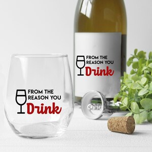 May include: A clear glass wine glass with the text "From the reason you drink" printed on it. The text is in black with the word "drink" in red. A wine bottle with a similar design is in the background.