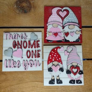 May include: Four Valentine's Day themed wooden signs. Two signs feature gnomes holding hearts, one with a red background and the other with a white background. The third sign says "There's gnome one like you" with hearts.