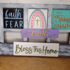 K&ouml;nnte beinhalten: Ein Holzschild mit einer abgenutzten wei&szlig;en Lackierung. Das Schild ist in vier separate Abschnitte mit unterschiedlichen Botschaften unterteilt. Der obere linke Abschnitt lautet "faith fear". Der obere rechte Abschnitt lautet "not today Satan". Der mittlere Abschnitt lautet "faith". Der untere Abschnitt lautet "Bless this home".