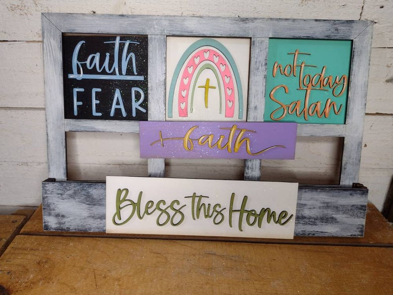 K&ouml;nnte beinhalten: Ein Holzschild mit einer abgenutzten wei&szlig;en Lackierung. Das Schild ist in vier separate Abschnitte mit unterschiedlichen Botschaften unterteilt. Der obere linke Abschnitt lautet "faith fear". Der obere rechte Abschnitt lautet "not today Satan". Der mittlere Abschnitt lautet "faith". Der untere Abschnitt lautet "Bless this home".
