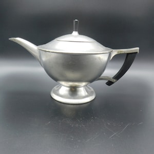 May include: A silver teapot with a black handle and a lid. The teapot has a round body and a wide spout.