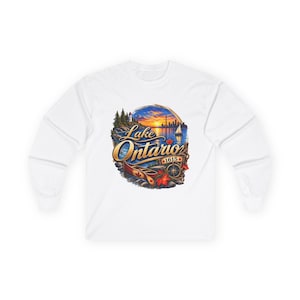 Peut inclure: Un t-shirt blanc à manches longues avec un motif coloré du lac Ontario au coucher du soleil. Le design comprend un canoë, une boussole, un phare, un voilier et le texte Lake Ontario 1615 avec une petite feuille d'érable rouge.