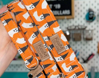 May include: Three orange and white dog collars with a ghost and witch hat pattern. The collars have a brown leather tag that says "K and M Collars".