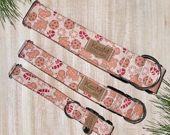 May include: Three dog collars with a gingerbread cookie and candy cane print. The collars are pink with brown gingerbread cookies, red candy canes, and white snowflakes. The collars have silver hardware and a brown leather tag that says "KandM Collars".
