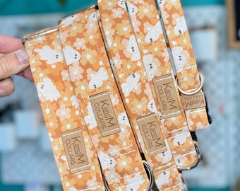 May include: Four orange and white dog collars with a ghost pattern and the text "KandM Collars" on each. The collars are stacked on top of each other.