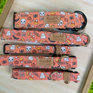 May include: Four orange and black dog collars with a Halloween theme. The collars feature ghosts, skulls, pumpkins, candy corn, and bats. The collars are made by KandM Collars.