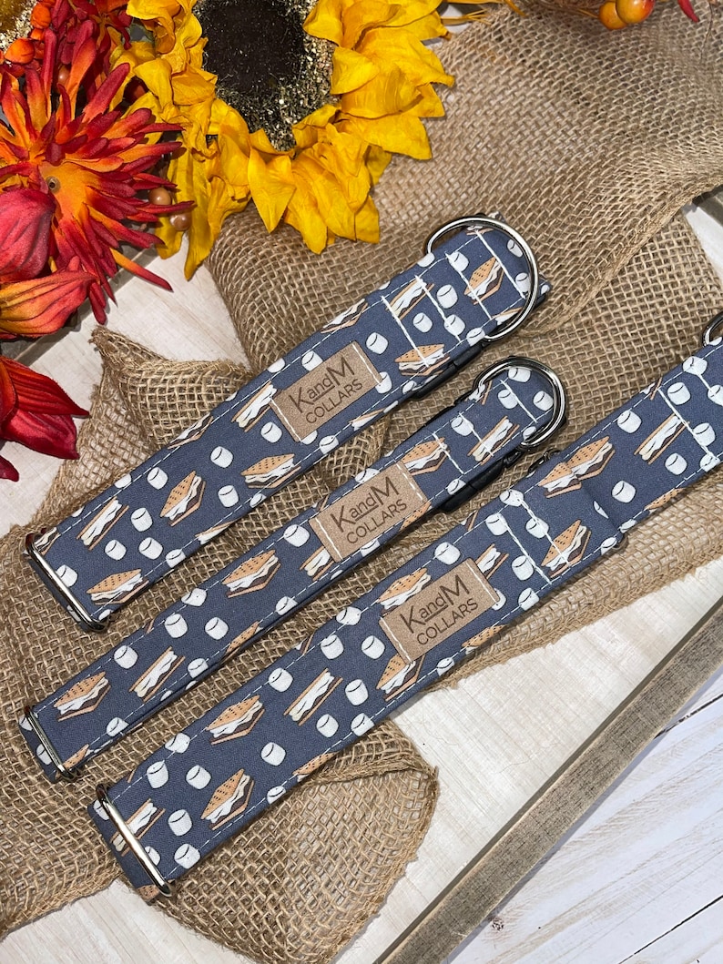 May include: Three dog collars with a blue background and a white print of graham crackers, chocolate, and marshmallows. The collars are labeled "Kang and M Collars".