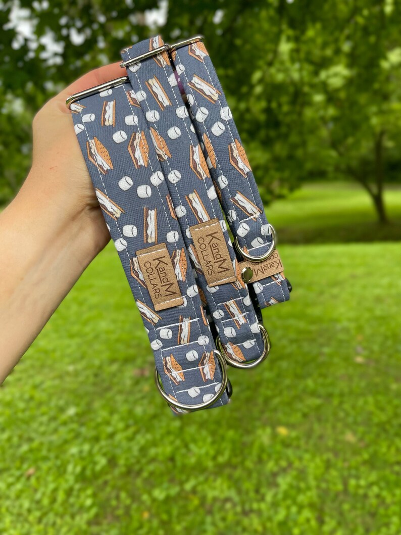 May include: Two dog collars with a blue background and a pattern of brown graham crackers and white marshmallows. The collars are made by K and M Collars.
