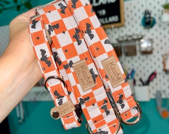 May include: Two orange and white dog collars with black bat silhouettes and white stars. The collars have a brown leather tag that says "K and M Collars".