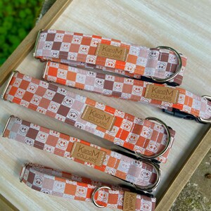May include: Five dog collars in different sizes with a checkered pattern featuring orange, brown, and white smiley faces. The collars are made by "KandM Collars".