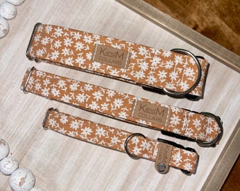 May include: Three dog collars with a white floral pattern on a brown background. The collars are made by "KandM Collars".