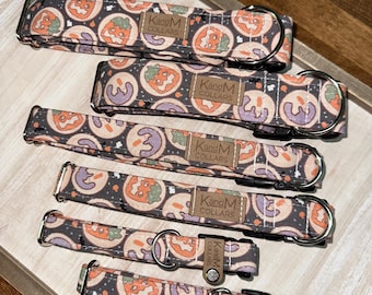 May include: Five different sizes of dog collars with a Halloween-themed print featuring orange and purple pumpkins on a black background. The collars are made by KangM Collars.