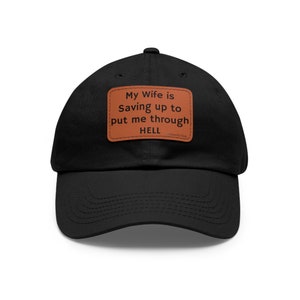 May include: Black baseball cap with a brown leather patch that says "My Wife is Saving up to put me through HELL" with the text "Sexist Guy" in smaller font below.