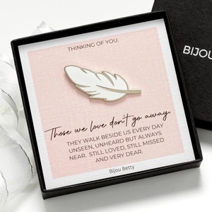 May include: A silver-toned feather pin inside a black gift box. The insert features the text: THINKING OF YOU. Those we love don't go away. THEY WALK BESIDE US EVERY DAY UNSEEN, UNHEARD BUT ALWAYS NEAR, STILL LOVED, STILL MISSED AND VERY DEAR. BIJOU BETTY.