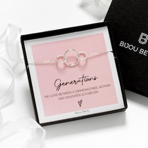 May include: A silver bracelet with three interlocking circles is displayed in a black box next to a black box with the text "BIJOU BETTY". The bracelet is on a pink card with the word "Generations" and the text "THE LOVE BETWEEN A GRANDMOTHER, MOTHER AND DAUGHTER IS FOREVER".