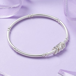 May include: A silver bangle bracelet with a series of small silver rings clustered together on one side.