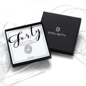 A silver 40th birthday necklace with four interlocking rings, presented in a black box with a white card that reads "Forty - Four rings for four decades" and "Bijou Betty".
