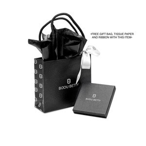 May include: A black gift bag and box set from Bijou Betty. The gift bag has a repeating "B" pattern and a white ribbon. The box and bag have the Bijou Betty logo. The bag is filled with black tissue paper.