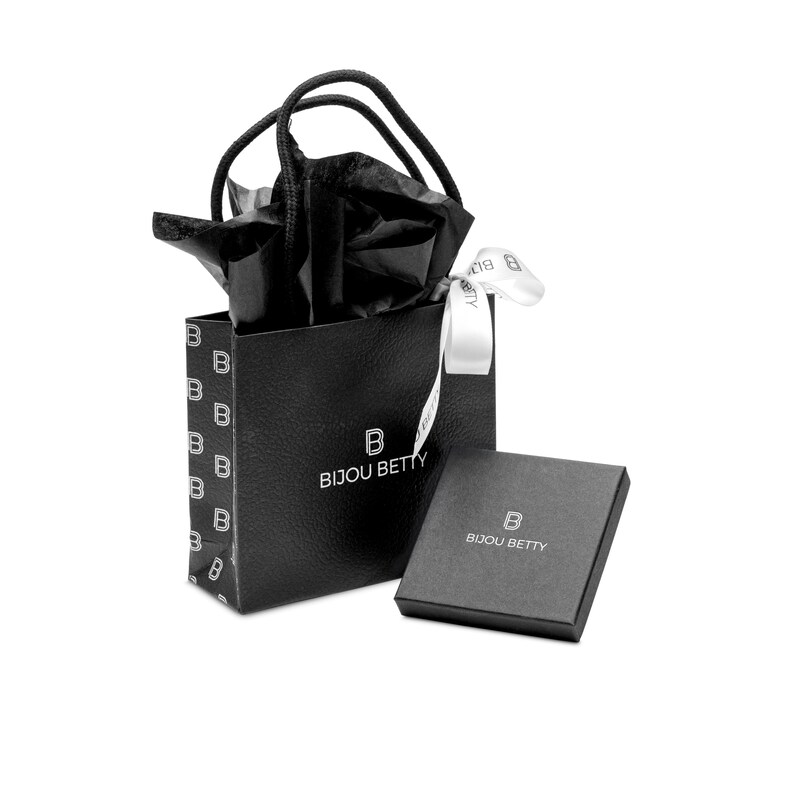 May include: A black gift bag with a repeating white letter B pattern, black handles, and black tissue paper, accompanied by a white ribbon and a square black jewellery box. Both the bag and the box feature the white text BIJOU BETTY with a B logo.