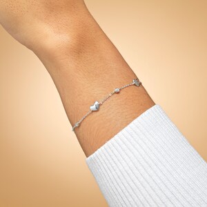 May include: A silver bracelet with a delicate chain and small heart charms. The bracelet has a single clear gemstone accent.