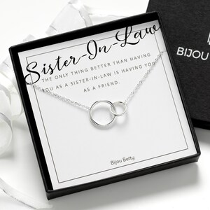 May include: A silver necklace with two interlocking circular rings displayed on a white card inside a black gift box. The card features the text: Sister-In-Law, The only thing better than having you as a sister-in-law is having you as a friend.