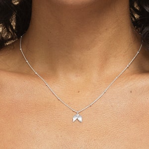 May include: A silver necklace with a delicate chain and a small angel wing charm.