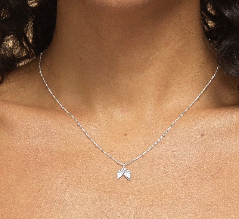 May include: A silver necklace with a delicate chain and a small angel wing charm.