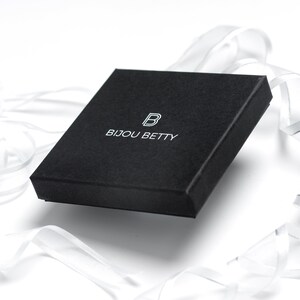 May include: A black square box with the text "Bijou Betty" and a stylized "B" logo printed in white.