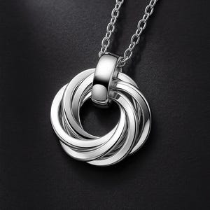May include: A silver-toned pendant necklace featuring a circular design composed of seven interlocking rings. The pendant is suspended from a matching silver-toned chain, with a polished, reflective metallic finish throughout the entire piece.