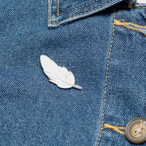 Enamel feather pin on denim jacket.