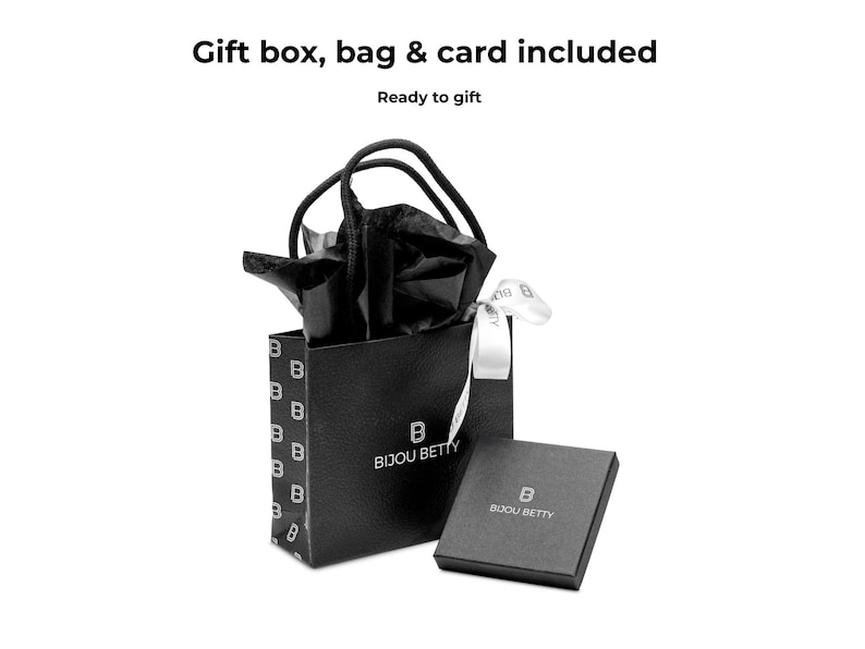 Pode incluir: Uma sacola de presente preta e uma caixa combinando, ambas com o logotipo "Bijou Betty", s&atilde;o apresentadas em um fundo branco. A sacola cont&eacute;m papel de seda preto e uma fita branca. O texto na parte superior diz "Gift box, bag & card included" e "Ready to gift."