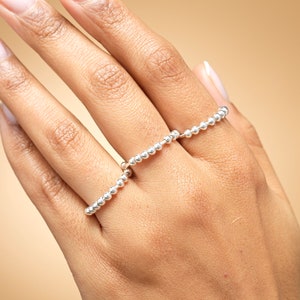 May include: Two silver rings, each constructed from a continuous series of small, polished metallic spheres. The rings feature a uniform, bead-like texture and a reflective, bright silver finish, worn on adjacent fingers to create a layered appearance.