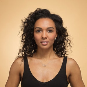 May include: A silver necklace featuring two small, interlocking circular rings as a pendant on a thin chain. The necklace is worn against a black vest top, highlighting the metallic finish and the simple, circular design of the jewellery piece.