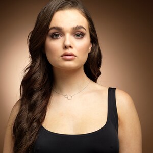 May include: A delicate silver-toned necklace featuring two small, interlocking circular pendants suspended from a thin chain. The necklace rests against the collarbone, showcasing a minimalist design with a polished metallic finish and a simple clasp.