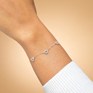 May include: A silver bracelet with a delicate chain and four small heart-shaped charms. Each charm is adorned with sparkling cubic zirconia stones.