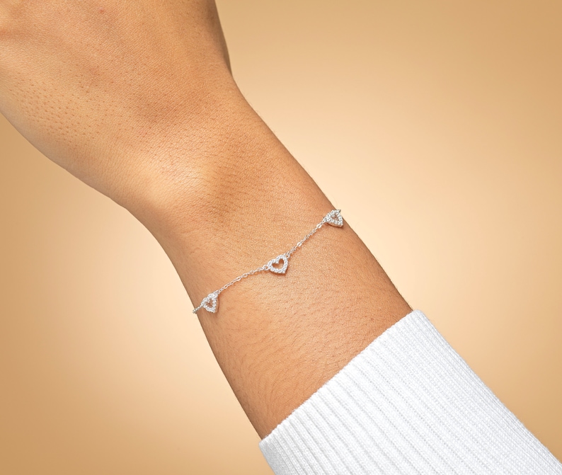 May include: A silver bracelet with a delicate chain and four small heart-shaped charms. Each charm is adorned with sparkling cubic zirconia stones.