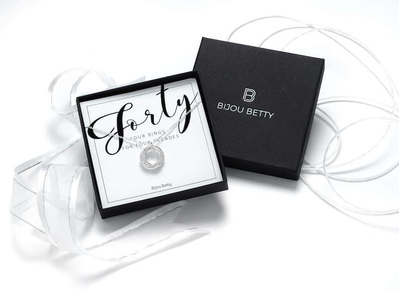 A silver 40th birthday necklace with four interlocking rings, presented in a black box with a white card that reads "Forty - Four rings for four decades" and "Bijou Betty".