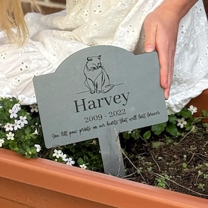 May include: A grey pet memorial garden stake featuring a cat illustration and the name "Harvey". The text includes the years 2009-2022 and the phrase "You left paw prints on our hearts that will last forever".
