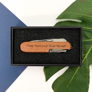 May include: A wooden pocket knife with a personalised message that reads "Poppy You're a cut above the rest!" The knife is in a black box with a black foam interior.