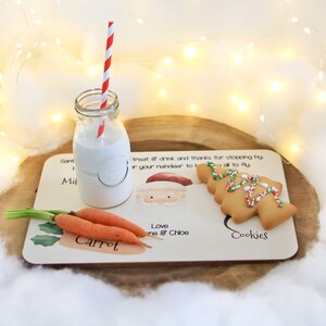 May include: A wooden tray with a Santa Claus illustration, a glass of milk with a red and white striped straw, a carrot, and a Christmas tree-shaped cookie. The tray has the text "Santa, Milk, Carrot, Cookies" and "Love one & Chloe".