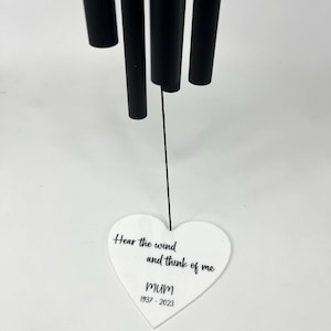 May include: Black wind chime with a white heart-shaped charm that reads "Hear the wind and think of me MUM 1937-2023".