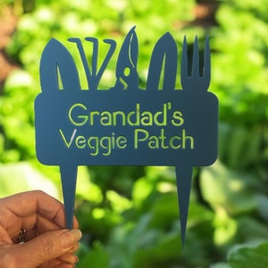 May include: A blue metal garden marker with a sign that reads "Grandad's Veggie Patch". The sign is decorated with cut-out images of gardening tools.