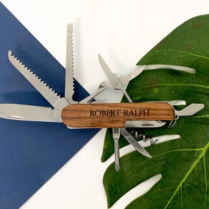 May include: A multi-tool pocket knife with a wooden handle engraved with the name "ROBERT RALPH". The knife features a variety of tools, including a blade, a saw, a screwdriver, and a bottle opener.