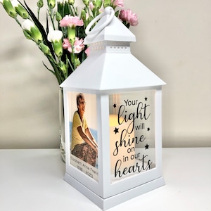 May include: White lantern with a photo of a woman and the text "Your light will shine on in our hearts" with stars around the text.