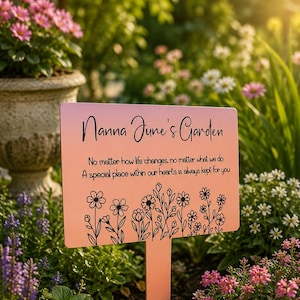 May include: A rectangular rose gold metal garden sign with a stake featuring the black text Nanna June's Garden and the quote No matter how life changes, no matter what we do A special place within our hearts is always kept for you with floral art.