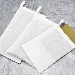 May include: Three white cotton muslin bags with drawstring closures. The bags are of different sizes and are arranged on a gray textured surface.