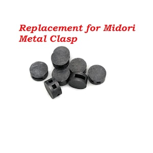 May include: A close-up of eight black metal clasps, designed to replace the clasps on a Midori Traveler's Notebook. The clasps are arranged in a pile on a white background.