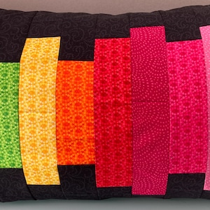May include: A rectangular cushion featuring a black background and vibrant vertical stripes. The stripes are in shades of turquoise, green, yellow, orange, red, pink, and purple. The stripes have varied patterns, suitable for home decoration.